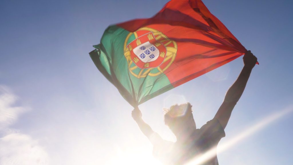 مرد جوانی پرچم پرتغال را بر فراز آسمان گرفته است که این تصویر برای عنوان همه بخوابید شهر در امن و امان است! انتخاب شده است.