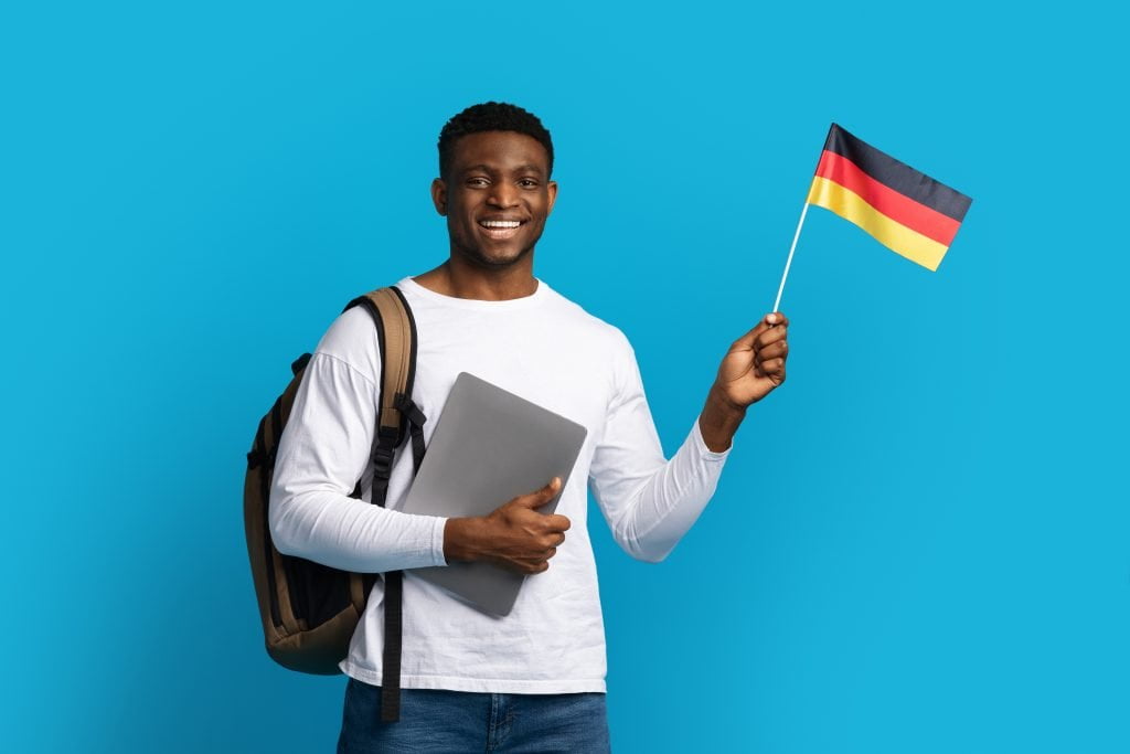 فردی سیاه پوست، به همراه لپ تاپ و کوله پشتی و پرچم اسپانیا برای عنوان ویزای متقاضی دانشجویی آلمان انتخاب شده است.