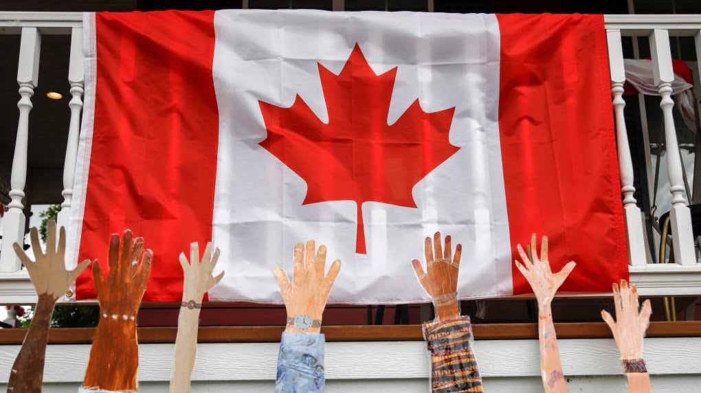 تصویری از دستان افراد با ملیت های متفاوت در مقابل پرچم کانادا برای عنوان کیفیت زندگی در کانادا انتخاب شده است.