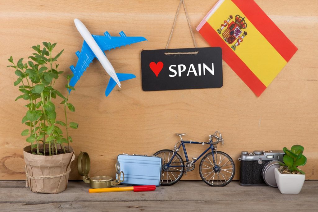 تصویری از پرچم اسپانیا به همراه نوشته ی اسپانیا و ماکت هواپیما برای عنوان چرا مهاجرت و تحصیل در اسپانیا؟ انتخاب شده است.