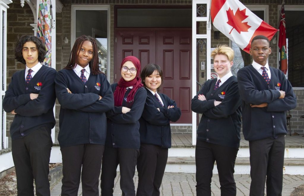 تصویری از دانش آموزان از ملیت های متفاوت در مقابل ورودی مدرسه‌ی شبانه روزی برای عنوان مدارس شبانه‌روزی انتخاب شده است.