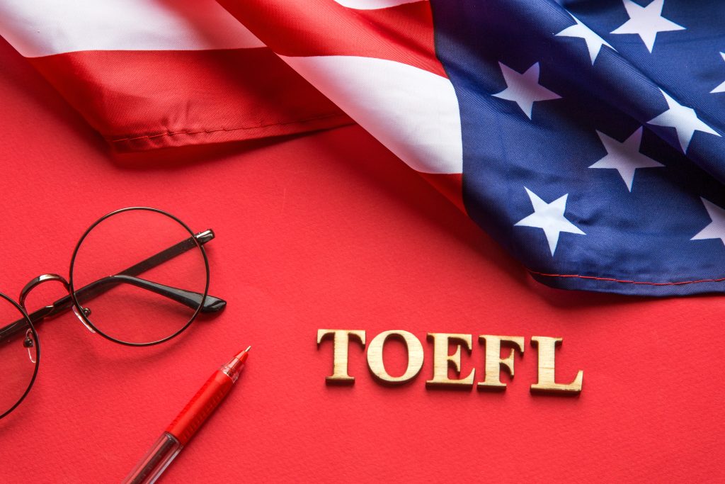 تصویری از نوشته‌ی تافل در کنار عینک و خودکار در کنار پرچم آمریکا برای عنوان مدرک تافل برای مهاجرت انتخاب شده است.