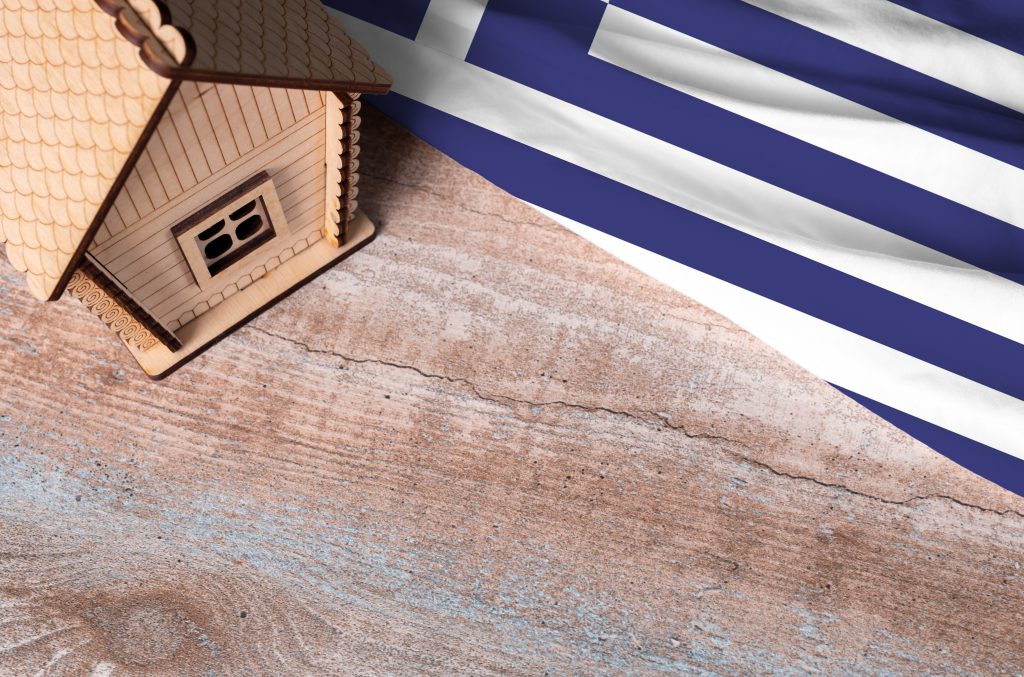 تصویری از یک ماکت خانه در کنار پرچم یونان برای عنوان خرید خانه در یونان یا اجاره ملک؟ انتخاب شده است.