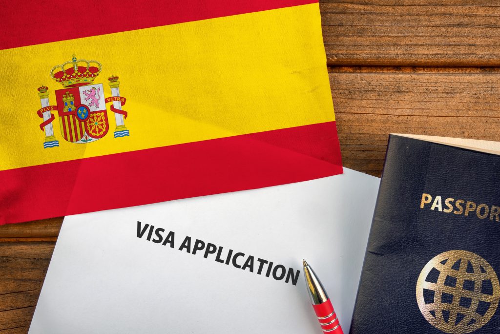 تصویری از فرم ویزا در کنار پرچم لسپانیا و پاسپورت برای عنوان انواع ویزاهای اسپانیا انتخاب شده است