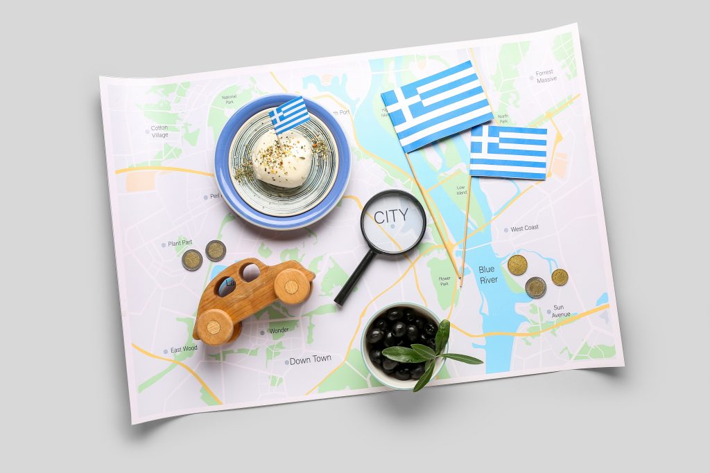 تصویری از نقشه یونان و پرچم این کشور و یک ماشین چوبی و چند سکه برای عنوان مدارک لازم برای اقامت در یونان از طریق خرید ملک انتخاب شده است.