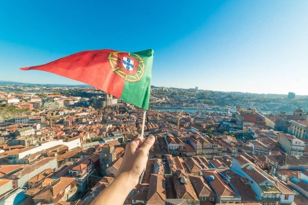 ساختمان های یکی از شهرهای کشور پرتغال به همراه تصویری از پرچم این کشور برای عنوان مزایای خرید ملک در پرتغال انتخاب شده است.